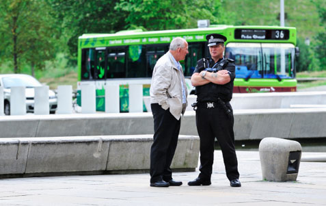 A policeman talking to a member of the public while standing on the paved area outside the main entrance to the Scottish Parliament.